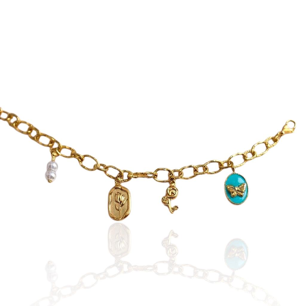 Bracelet Valmira avec petites perles blanches, médaillon tulipe, breloque rose et médaillon papillon sur fond turquoise